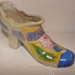 May include: A ceramic shoe planter with a blue, yellow, green, and purple floral design. The shoe has a high heel and a pointed toe.