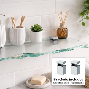 May include: A clear glass bathroom shelf with a natural edge, displayed against white tile. The shelf holds a white soap dispenser, toothbrush holder, small plant, and a diffuser. Chrome matt aluminum brackets are included.