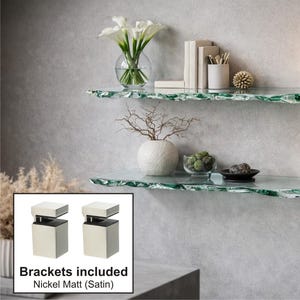 Puede incluir: Dos estantes de vidrio transparente con un borde orgánico único están montados en una pared gris. Los estantes están decorados con un jarrón de flores blancas, libros, velas y objetos decorativos. Soportes Nickel Matt (Satin) incluidos.