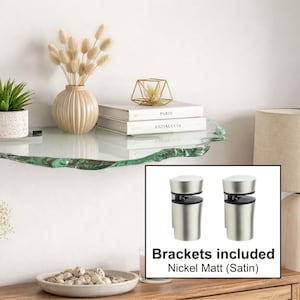 Puede incluir: Una estantería de vidrio transparente con un borde natural e irregular está montada en una pared blanca. La estantería contiene una pequeña planta en maceta, un jarrón con flores secas, libros y un objeto geométrico decorativo. Los soportes incluidos son de níquel mate.