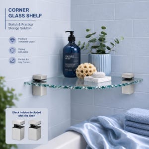 May include: A clear tempered glass corner shelf with a textured edge, mounted with two metallic square brackets. The shelf holds a dark blue soap bottle labelled meraki, a textured beige sponge, and a small plant in a light blue ribbed pot.