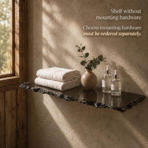 Può includere: Una mensola nera con bordo ruvido e testurizzato che sostiene due asciugamani bianchi piegati, un vaso beige con foglie verdi e due flaconi a pompa in vetro trasparente. Testo: Shelf without mounting hardware. Choose mounting hardware must be ordered separately.