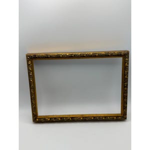 May include: A rectangular picture frame with a metallic gold finish. The frame features an ornate, raised relief pattern along all four sides, characterised by repeating scrollwork and leaf-like motifs that create a textured, decorative border.