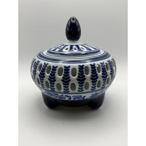May include: A blue and white ceramic incense burner with a lid and three small feet. The body features a pierced design with leaf-like cutouts. The lid has a knob and a pierced pattern. The overall design is a classic, decorative style.