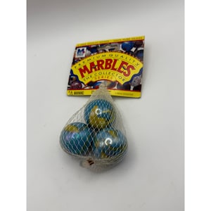 Puede incluir: Una bolsa de red que contiene tres canicas azules y amarillas. Las canicas tienen un patrón arremolinado. Una etiqueta de cartón encima de la red dice "Premium Quality Marbles The Collector Series". Las canicas son tiradores de 2,5 cm.