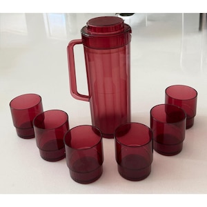 Può includere: Un set di vetreria colorata di rosso, tra cui una caraffa con coperchio e manico, e sei bicchieri. I bicchieri hanno un design angolato distintivo. Il set è realizzato in materiale traslucido. Ideale per servire bevande.