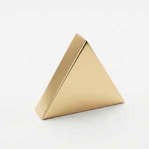 K&ouml;nnte beinhalten: Eine goldfarbene, dreieckige Schachtel mit gefaltetem Deckel. Die Schachtel besteht aus einem gl&auml;nzenden, metallischen Material und steht auf einer wei&szlig;en Oberfl&auml;che. Die Schachtel hat eine geometrische Form, und die Gesamt&auml;sthetik ist minimalistisch und modern.