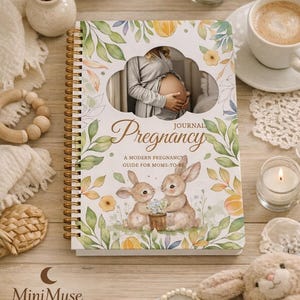 Peut inclure: Un journal de grossesse à spirales avec une photo d'une femme enceinte et le mot "Pregnancy". La couverture présente des illustrations de lapins et de fleurs. L'image comprend des bougies, une tasse de café et un jouet en peluche.