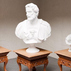 Peut inclure: Trois bustes classiques blancs sur des socles en bois ornés. Le buste central représente un homme barbu, flanqué de bustes de femmes de chaque côté. Les socles ont des pieds sculptés et des dessus carrés, ajoutant une touche d'élégance.