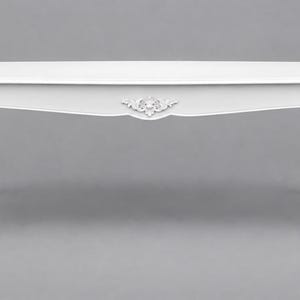 May include: A rectangular white coffee table featuring a smooth flat top and four curved cabriole legs. The apron of the table is decorated with a central carved floral motif, and the legs also feature carved detailing along their length.