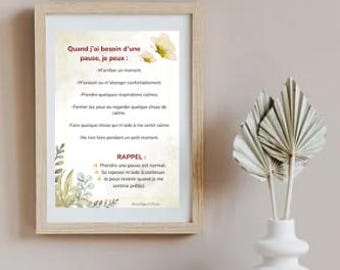 May include: A framed print with French text, displayed on a white surface. The print has a light wood frame and features text in red and black. A white vase with dried decorative leaves is to the right of the frame. The background is a neutral color.
