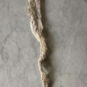 Könnte beinhalten: Eine abgeworfene Schlangenhaut, hellbeige mit braunen Markierungen, liegt auf einer grauen Oberfläche. Die Haut ist lang und schlank, mit einem strukturierten, schuppenartigen Muster. Die Schlangenhaut ist gewellt und verdreht.