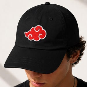 May include: Black baseball cap with a red cloud design embroidered on the front. The cloud has a white outline. The cap has a curved brim and a button on top.