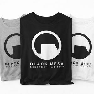 May include: Three t-shirts in gray, black, and white, each featuring a circular logo with a geometric design and the text "BLACK MESA RESEARCH FACILITY". The shirts are folded and displayed against a white background.