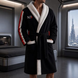 Puede incluir: Bata de baño negra con ribete blanco y una franja blanca, roja y negra en la manga. La bata tiene cuello chal y cinturón anudado. Las letras "N7" están impresas en el pecho.