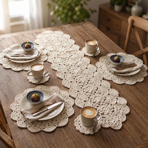 Könnte beinhalten: Ein cremefarbener Häkel-Tischläufer mit passenden runden Platzdeckchen mit gewelltem Rand. Das Set enthält kleine runde Häkel-Untersetzer, Keramikteller mit Blumenmuster, Leinenservietten, Metallbesteck und kleine Schalen mit Feigen.