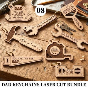 May include: A selection of laser-cut wooden keyrings in various shapes, including a hat, spanner, hammer, saw, tape measure, and a controller. Text includes "DAD", "YOU ARE THE BEST", and "Happy Fathers Day".