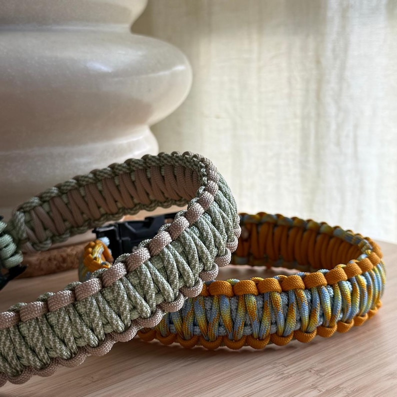 Peut inclure: Deux bracelets en paracorde. L'un est vert olive et beige, l'autre est jaune, bleu et orange. Les bracelets sont faits de cordons tiss&eacute;s serr&eacute;s et sont probablement faits &agrave; la main. Les bracelets sont sur une surface en bois.