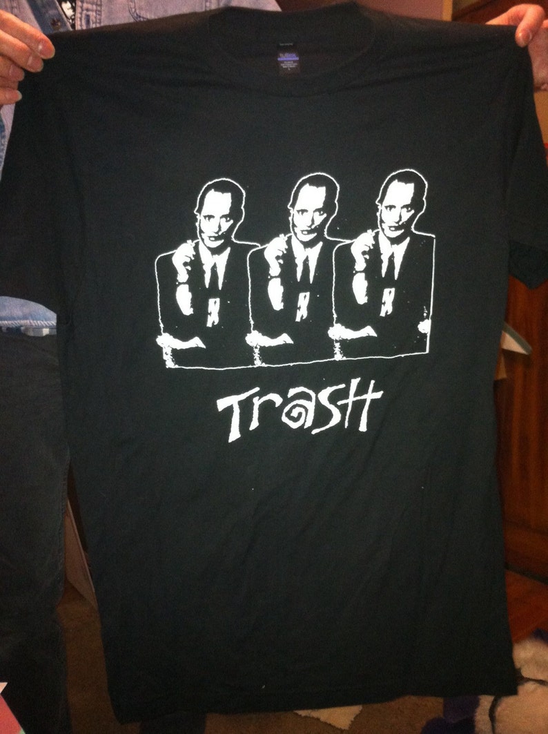May include: Black t-shirt featuring a white graphic of three men in suits with the word "Trash" printed below.
