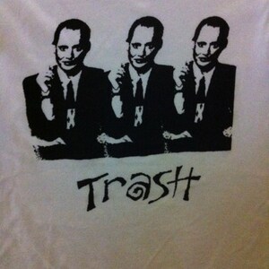 Op de afbeelding: Zwart-wit grafisch T-shirt met drie mannen in pak met de tekst "#SSST" gedrukt op de voorkant.