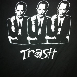 May include: Black and white graphic t-shirt featuring three men in suits with the word "Trash" printed below them.