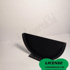 May include: A black, semi-circular 3D-printed object with a flat base. The object has a smooth, matte finish. A green sticker with the word "LICENSE" and other text is in the lower right corner.