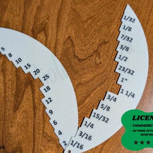 May include: Two white, semi-circular tools with black markings for measurements. One tool has numbers 1 through 25, and the other has fractions like 1/32, 1/8, and 1 1/4. The tools are on a wooden surface. A green license badge is in the corner.