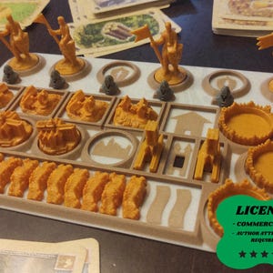 May include: A board game organizer with various orange game pieces, including figures, castles, and walls. The organizer is beige and has slots for each piece. Game cards are visible in the background. A green sticker with the word "LICENSE" is in the bottom right corner.