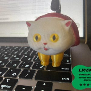 Pode incluir: Uma figura de gato extravagante com capuz vermelho e pernas amarelas está em um teclado de laptop. O gato tem olhos amarelos grandes e uma boca vermelha pequena. O teclado tem teclas pretas com letras brancas. Um distintivo de licença verde está no canto inferior direito.