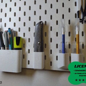 Op de afbeelding: Een witte pegboard met diverse knutselspullen. Inclusief pennen, potloden, een hobbymes en hobbymessen in witte houders. Een schaar en een blauw gereedschap hangen aan het bord. Een groen licentiebadge staat rechtsonder.