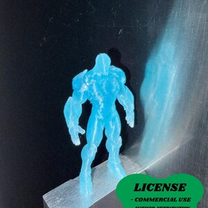 May include: A translucent blue figurine of a muscular humanoid figure. The figure is standing on a small, silver block. The image includes a green badge with the word "LICENSE" and text below it. The figure is approximately 3 inches tall.