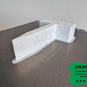 以下が含まれることがあります： グレーの表面に、白の3Dプリントされた文字「T」。 文字は積み重ねられた層でできており、小さなベースが付いています。 「LICENSE」という単語とテキストが入った緑色のバッジが右下にあります。