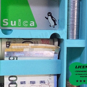 Peut inclure: Un organisateur bleu clair avec des compartiments pour la monnaie, les pièces de monnaie et une carte Suica. La carte Suica est verte avec le mot "Suica" et une illustration de pingouin. L'organisateur contient également du papier-monnaie et une pile de pièces.