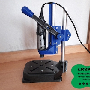 Pode incluir: Uma furadeira azul e preta com uma ferramenta rotativa Dremel conectada. A furadeira tem uma base preta e uma estrutura de suporte azul. A imagem também inclui um distintivo verde com a palavra "LICENSE" e quatro estrelas.