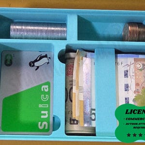 May include: A light blue organiser with compartments containing coins, rolled-up currency, and a Suica card with a penguin graphic. The card has a green section and the word "Suica".