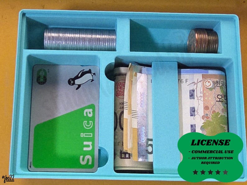 May include: A light blue organiser with compartments containing coins, rolled-up currency, and a Suica card with a penguin graphic. The card has a green section and the word "Suica".