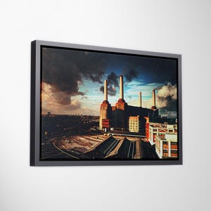 Può includere: Stampa su tela incorniciata raffigurante un paesaggio industriale con una grande centrale elettrica. L'opera d'arte raffigura un edificio in mattoni con alti camini contro un cielo nuvoloso. La stampa è racchiusa in una cornice grigio scuro.