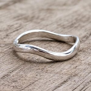 May include: A silver ring with a flowing, wavy design. The ring has a smooth, polished surface and an organic shape. The ring is shown on a wooden surface.