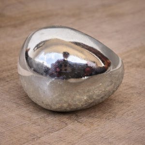 May include: A smooth, silver-colored, egg-shaped decorative object. The reflective surface mirrors the surrounding environment. The object is placed on a wooden surface, creating a contrast between the textures.