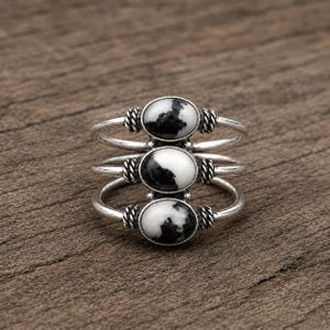Può includere: Un anello in argento con tre fasce sovrapposte, ciascuna incastonata con una pietra ovale bianca e nera. Le pietre sono tenute in posizione da montature in argento con dettagli a corda intrecciata su entrambi i lati di ogni gemma ovale.