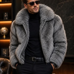 May include: A grey faux fur jacket with a large collar and a front zipper closure, worn over a black turtleneck sweater and black trousers with a black leather belt. The jacket features a thick, textured pile in shades of charcoal and silver.
