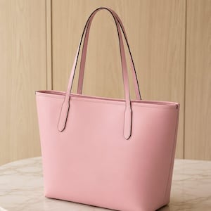 May include: A solid light pink tote bag with a smooth finish, featuring two thin shoulder straps attached to the top edge. The bag has a rectangular shape with a flat base and clean, minimalist lines, showcasing a consistent pastel pink color throughout.
