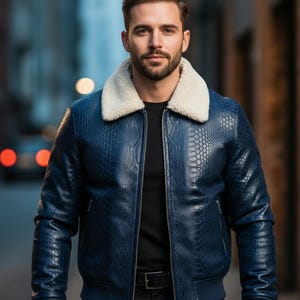 Puede incluir: Chaqueta bomber de cuero azul con cuello de borreguillo blanco. La chaqueta tiene un patrón texturizado similar a la piel de reptil y cierre de cremallera. La chaqueta tiene dobladillo y puños de canalé.