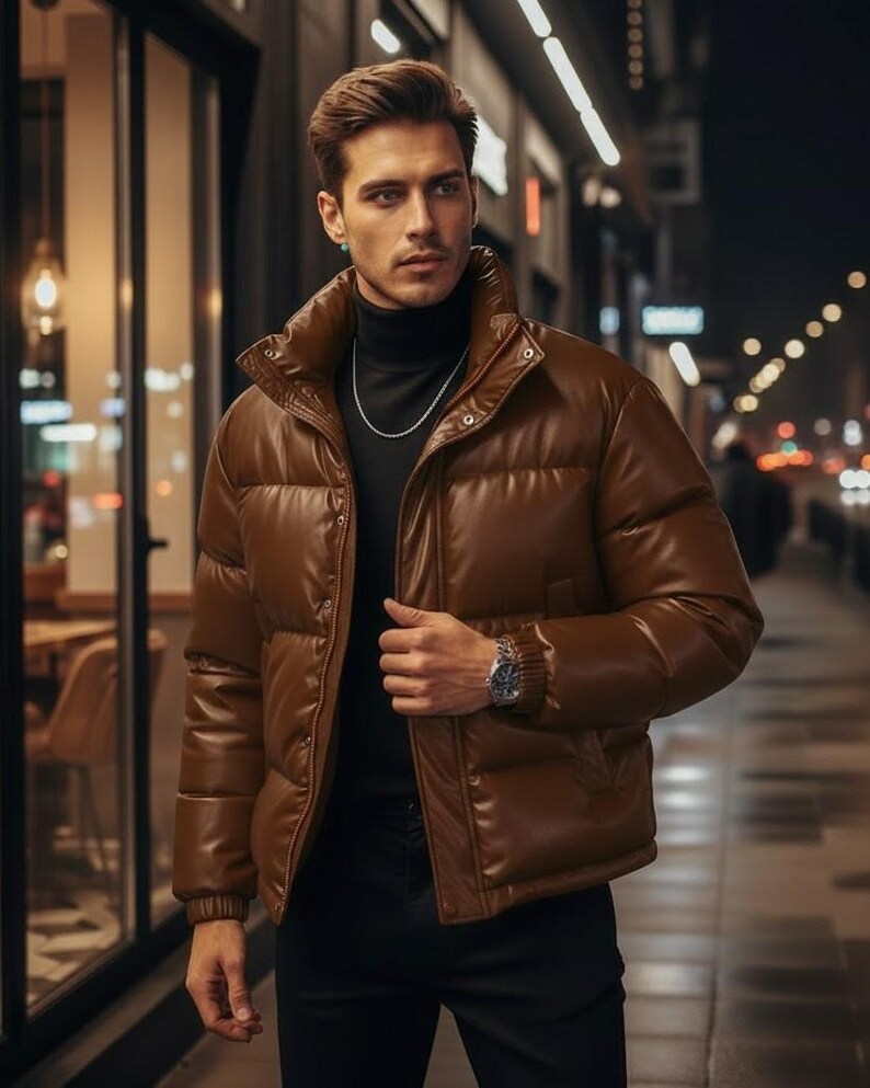 May include: A brown puffer jacket with a high collar. The jacket has a quilted design and a front zipper closure. The person is wearing a black turtleneck and a silver chain necklace. The background is a city street at night.