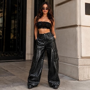 May include: A black lace strapless crop top paired with high-waisted black cargo pants featuring a glossy, textured crocodile-skin pattern. The pants have wide legs and large side pockets, while the top is a fitted, semi-sheer lace garment.