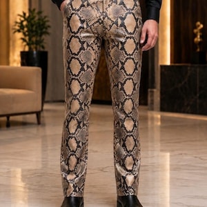 Puede incluir: Pantalones largos con un patrón de piel de serpiente en tonos beige y negro. Los pantalones tienen un corte ajustado, una cintura estándar con trabillas para cinturón y cierre de botón frontal. Se combinan con un cinturón y zapatos negros.