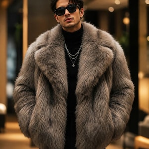 May include: A thick, grey faux fur jacket with a wide lapel collar, worn over a black turtleneck jumper. The outfit includes a layered silver chain necklace with a cross pendant and dark-tinted sunglasses with black frames.