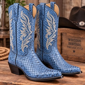 May include: A pair of blue cowboy boots featuring a textured snakeskin pattern and intricate cream-colored stitching in a flame-like design on the shaft. The boots have a pointed toe, a stacked heel, and pull tabs at the top of the shaft.
