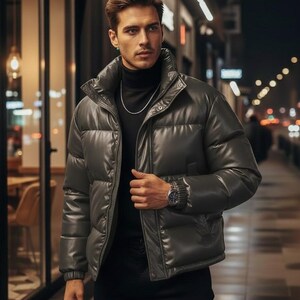 May include: A dark gray puffer jacket with a high collar and a shiny finish. The jacket is worn over a black turtleneck and paired with black pants. A silver chain and watch complete the look. The background shows a city street at night.