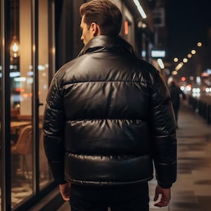 May include: A black puffer jacket with a shiny, leather-like appearance. The jacket has horizontal stitching and a high collar. The person is walking on a sidewalk at night, with storefronts and streetlights in the background.